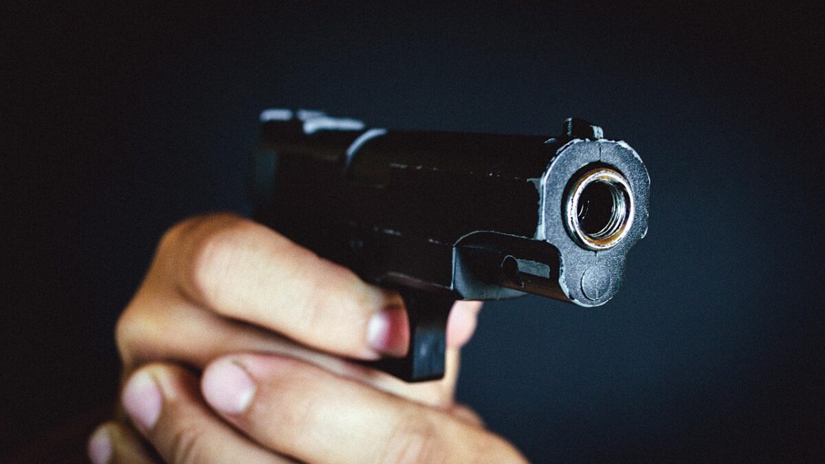 Gros plan sur un pistolet noir tenu à la main, pointé vers l'objectif, sur fond sombre.