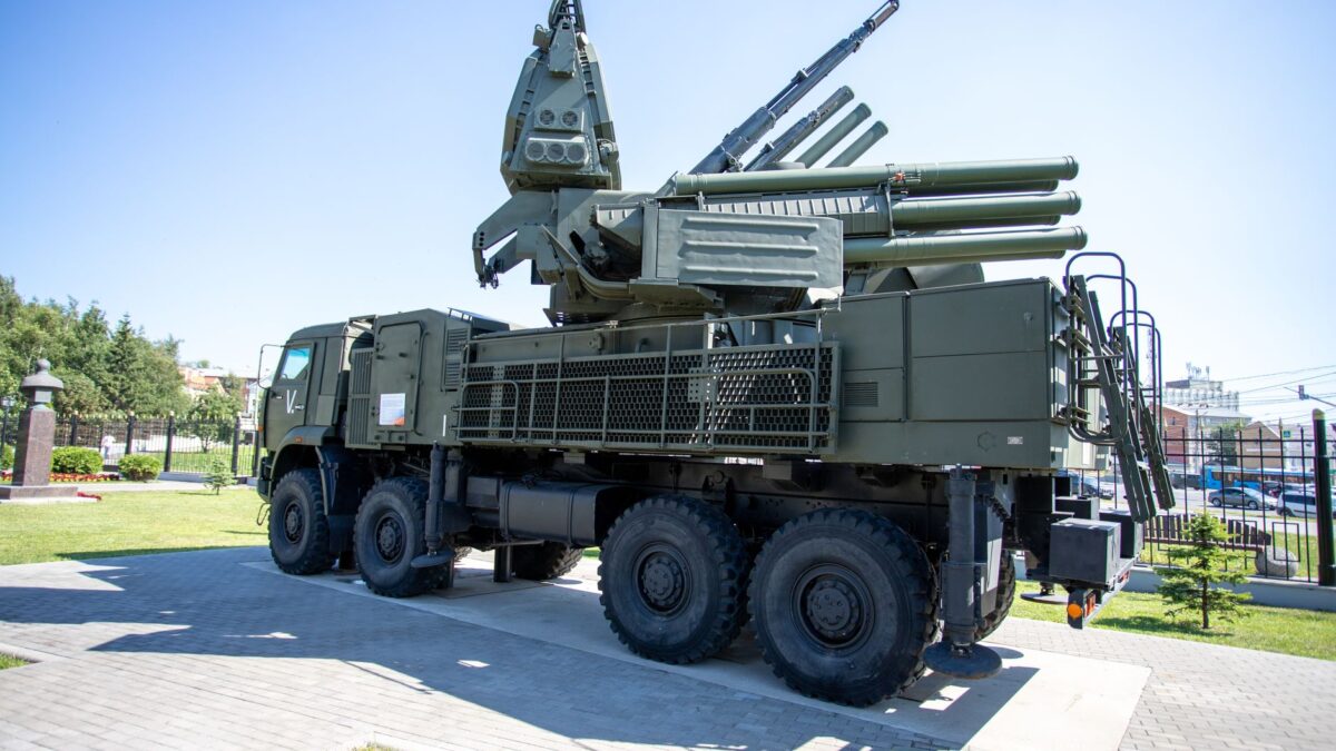Système antiaérien Pantsir-S1 sur châssis de camion militaire à 8 roues, vert kaki, exposé en extérieur sur un dallage ensoleillé, avec clôture métallique, arbres et pelouse en arrière-plan.