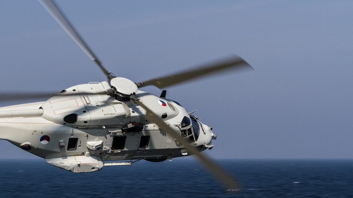 Hélicoptère militaire blanc en vol au-dessus de la mer, rotor à quatre pales flou, cocardes rouge, blanc et bleu sur le fuselage.
