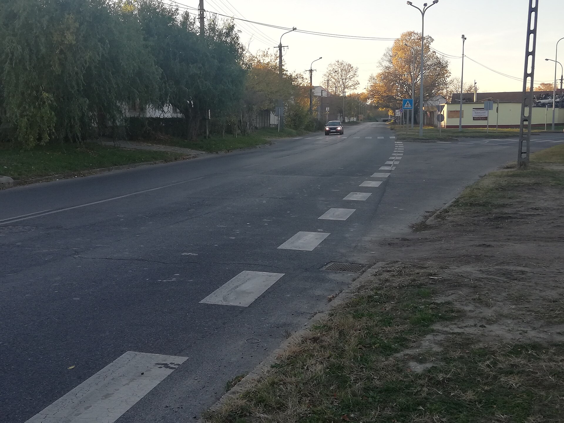 A quiet road leaving Nagykőrös towards Budapest at dusk, with a single car approaching