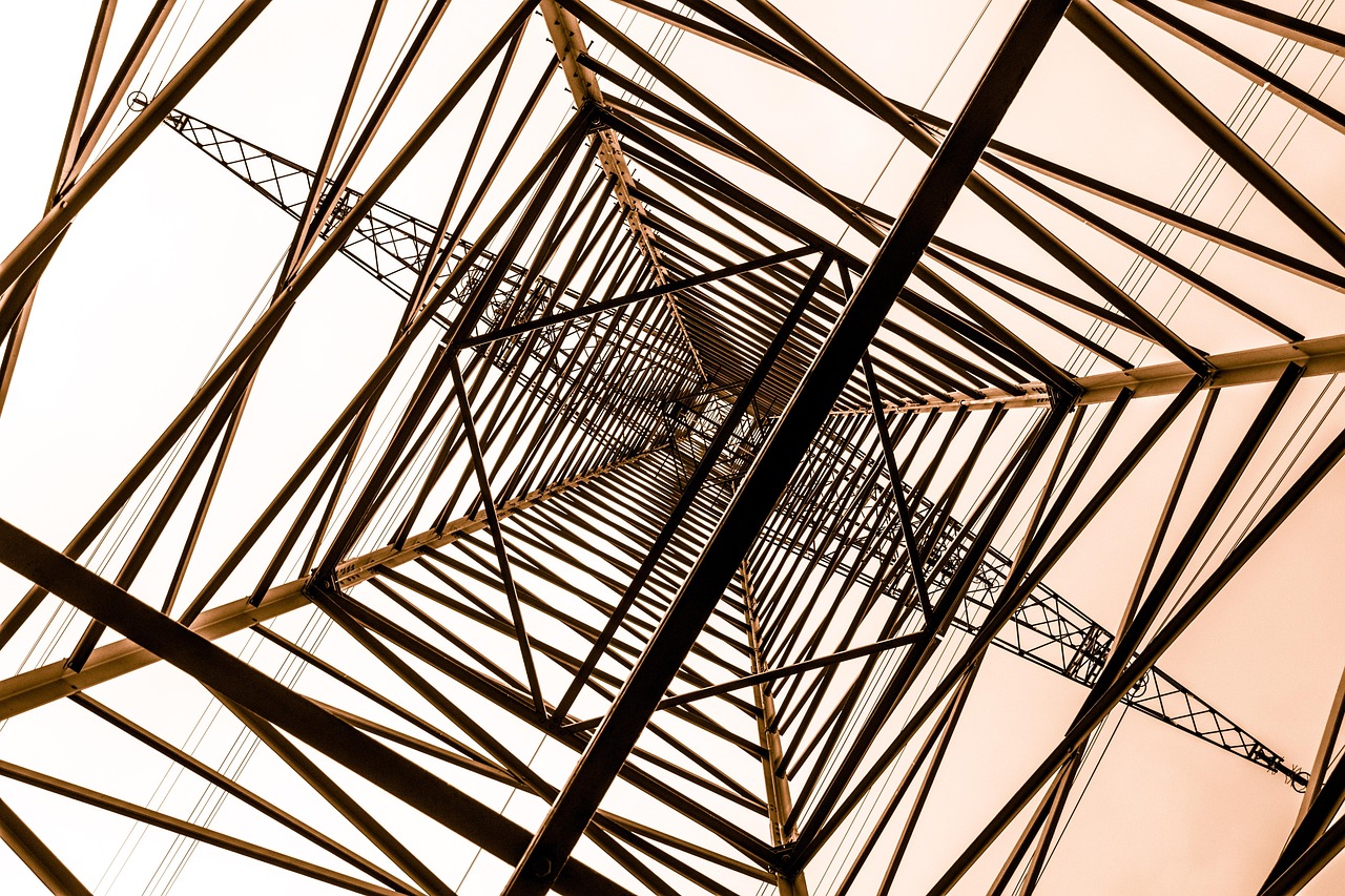 Steel lattice of an electricity pylon seen from below, with power lines crossing a pale sky